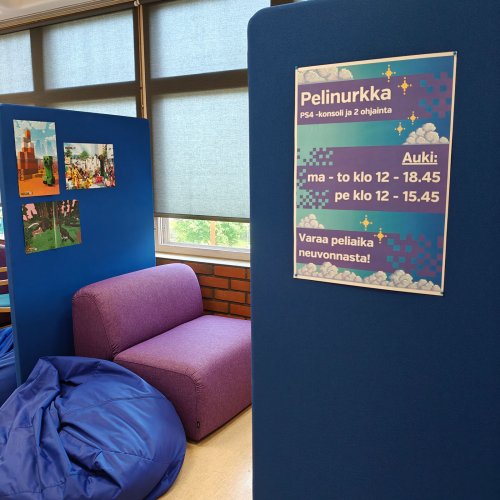 Kuva pelinurkasta. Kuvassa violetti nojatuoli, sininen säkkituoli ja kaksi sinistä sermiä. Ikkunasta näkee ulos ja sermissä lukee pelinurkan aukioloajat.