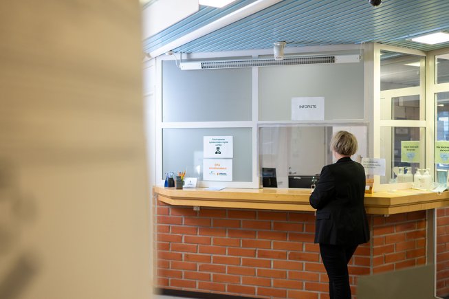 Nainen seisoo vastaanottopöydän äärellä selin kameraan. Kuvassa näkyy kaistale työkkärin aulaa.