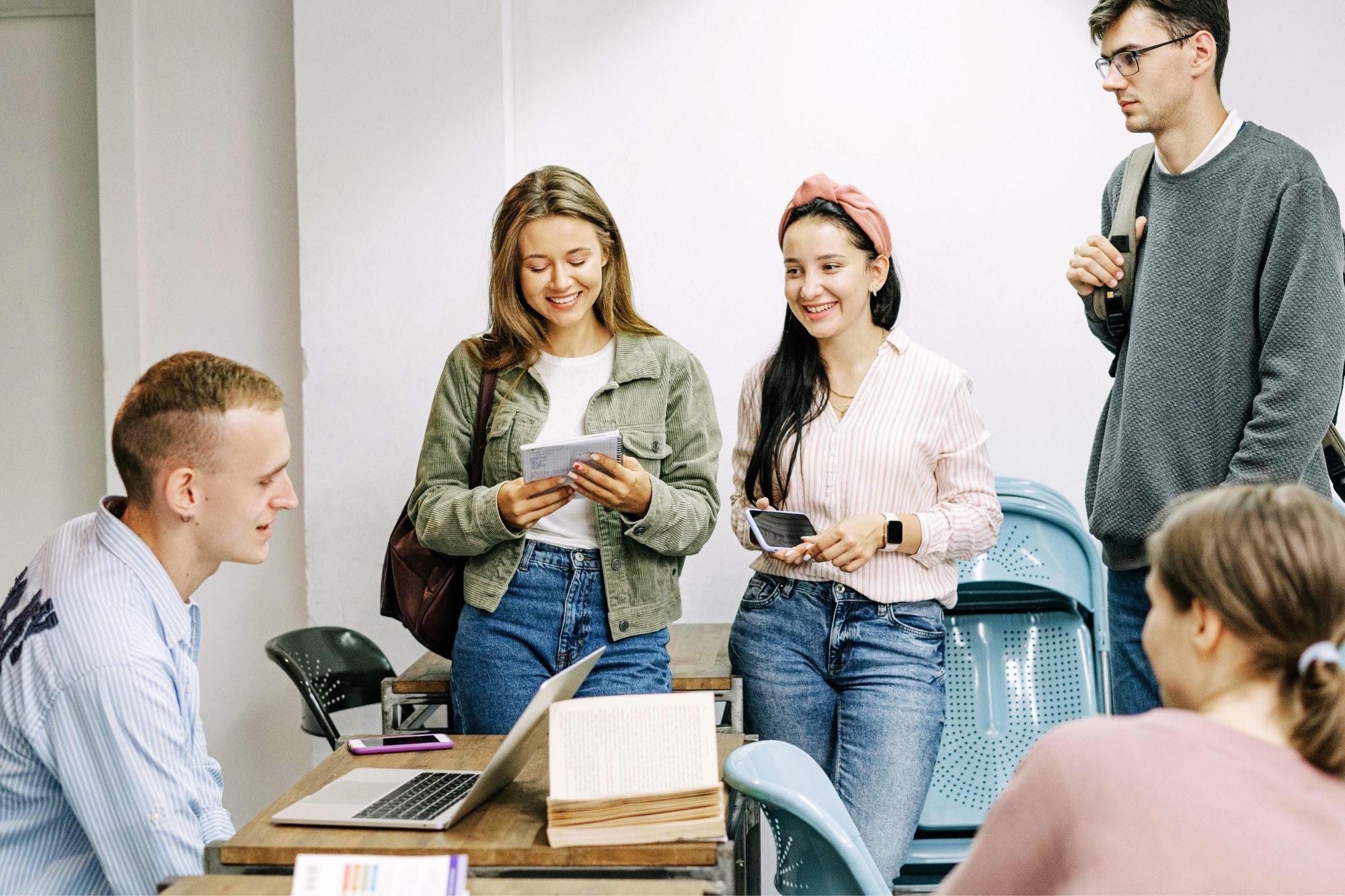 Joukko nuoria ihmisiä seisoskelee pöydän ympärillä ja hymyilee.