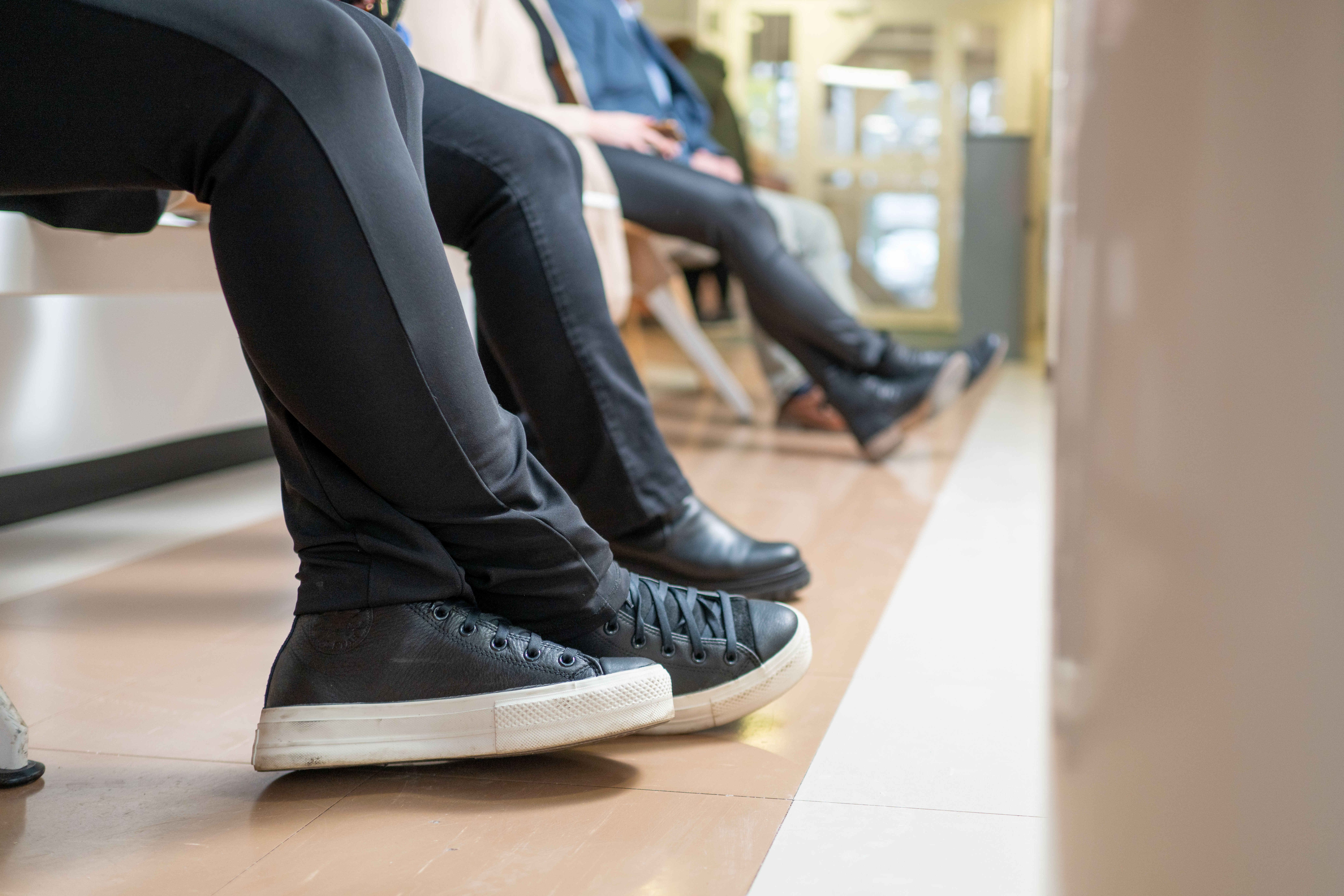 Jalkoja rivissä. Henkilöt istuvat penkillä.