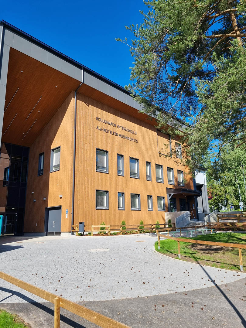 Koulu kesäisessä aurigonpaisteessa, kiveyksellä pudonneita männykäpyjä