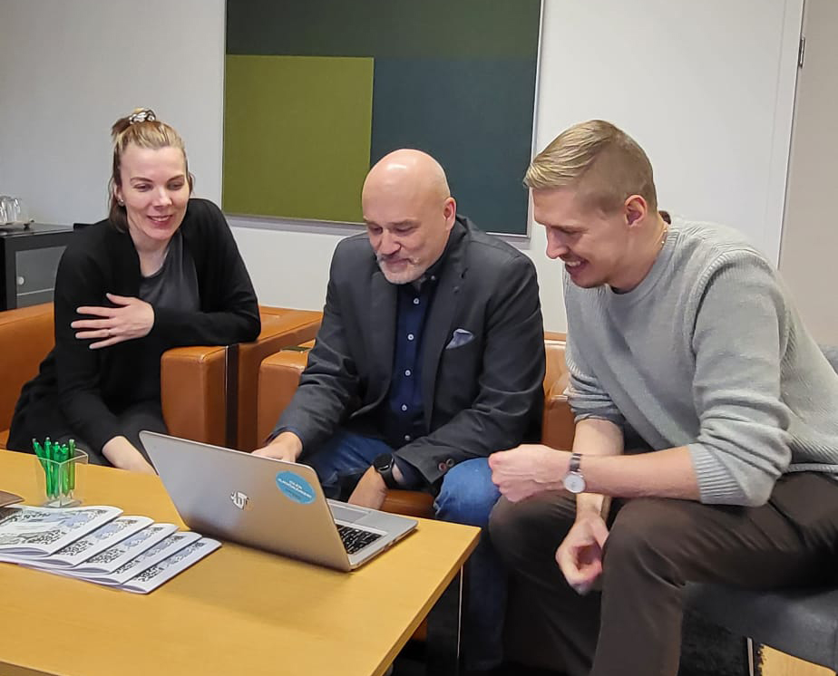 Kolme henkilöä katsoo tietokonetta ja hymyilee.